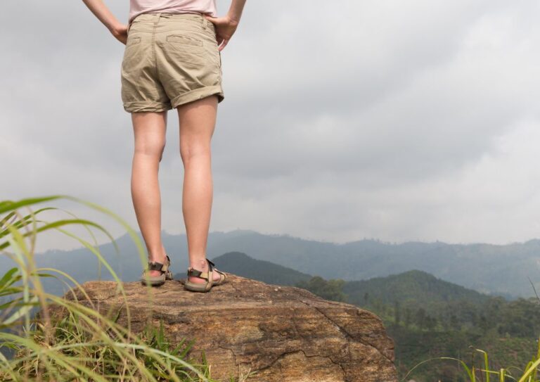 A man standing on a rock looking out into nature wearing Tevas for hiking.