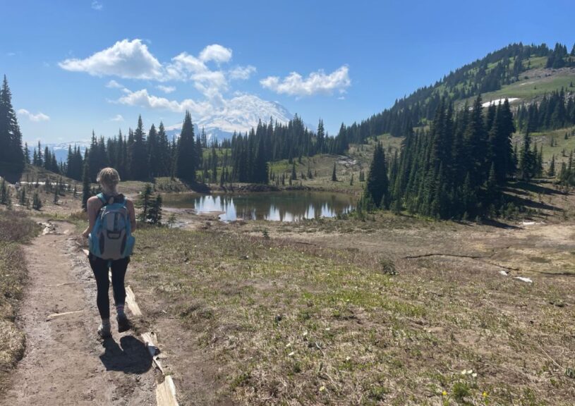 Myself walking on a dirt path near a pond with mountains in the background.