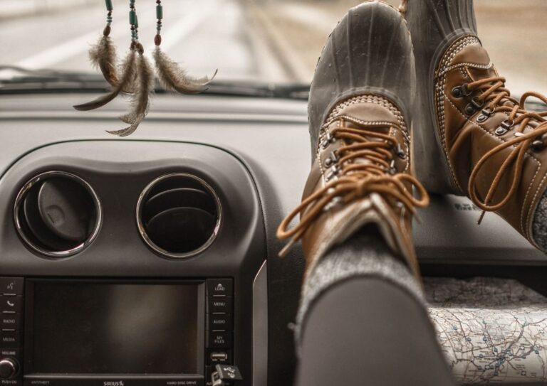 A person wearing a pair of duck boots on the dash of a car.