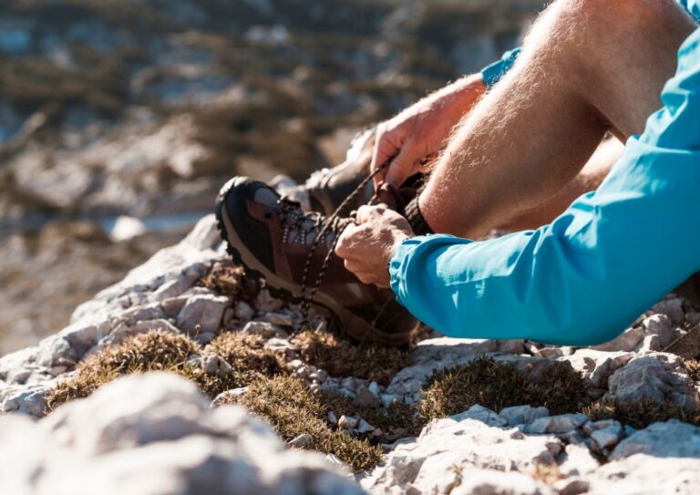 A person wearing a blue coat tieing their hiking boots that are neither too big nor too small