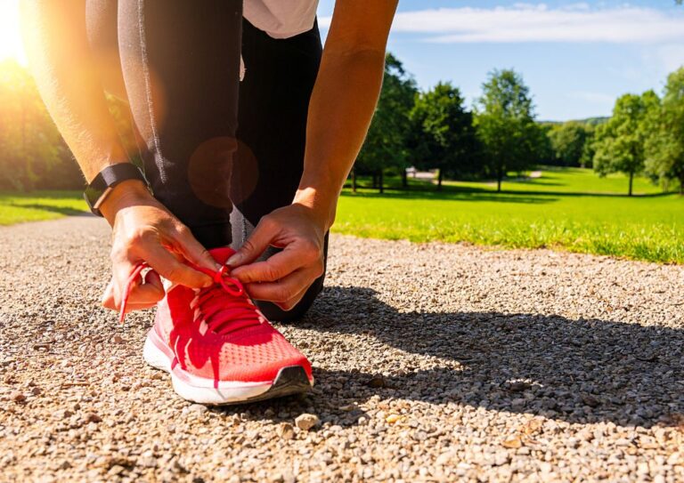 A person tieing a pair of pink running shoes on a dirt hiking trail