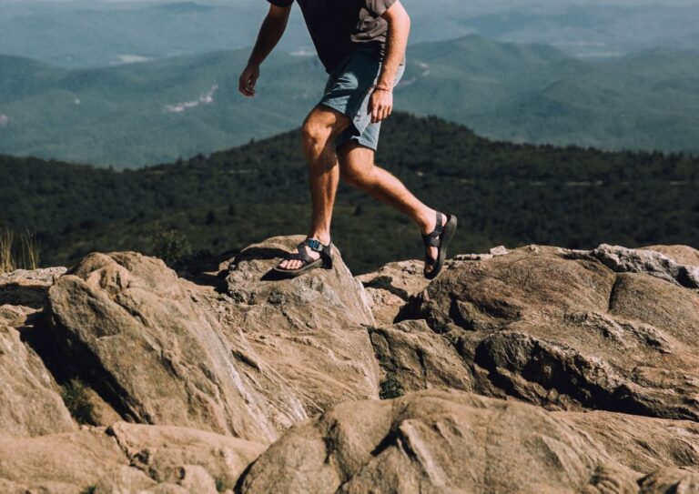 A person walking on rocks wearing a pair of Chacos hiking.