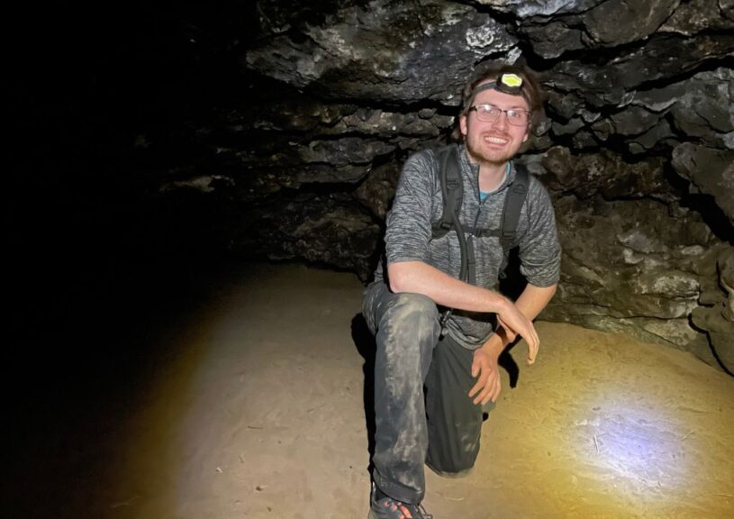 Tyler in a cave with dirty pants and a headlamp on.