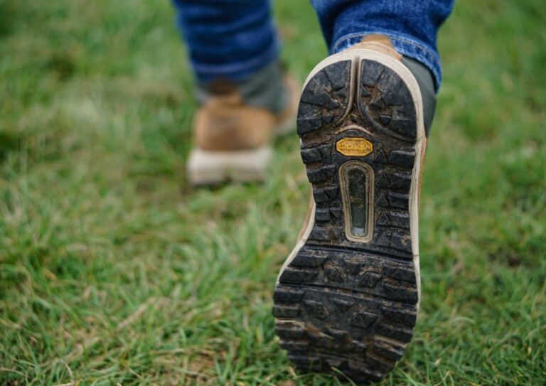 A pair of hiking boots that have been broken in, walking on a field of grass.