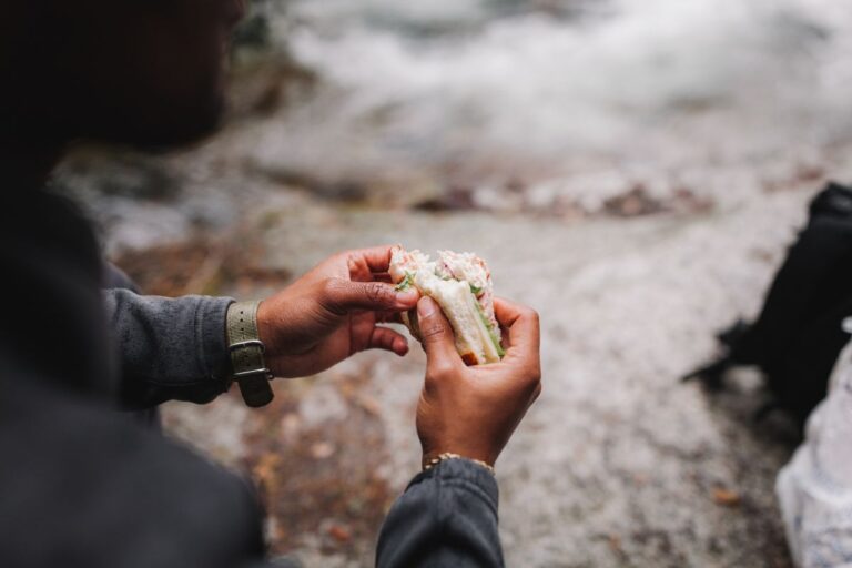 A person holding a sandwich fulfilling their hiking nutrition.
