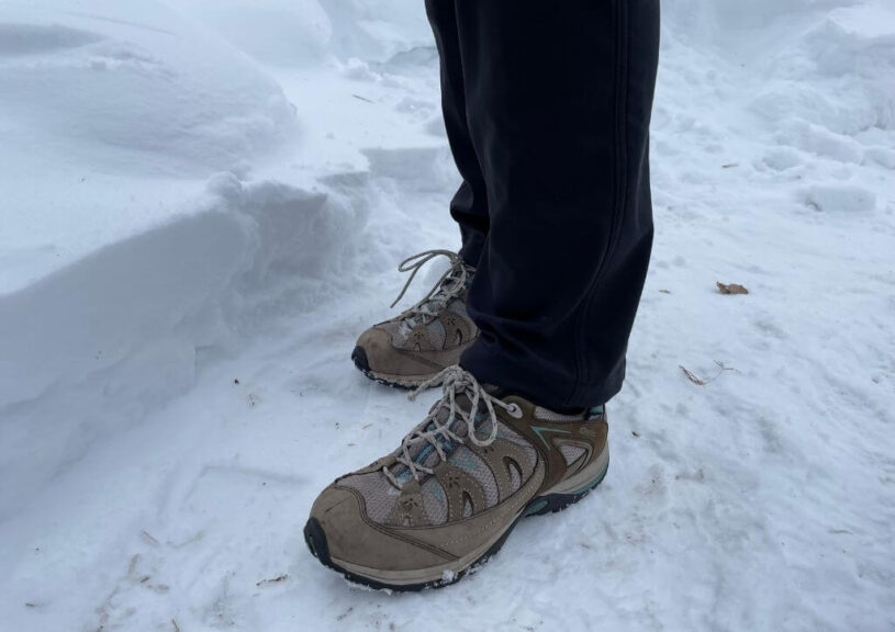 Myself wearing a pair of hiking boots on a trail covered in packed snow.