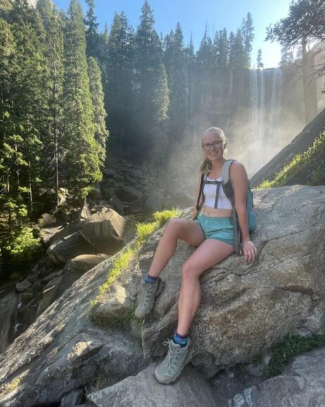 Myself on a rock with a waterfall behind me, wearing my favorite hiking boots that don't cause sore feet after.