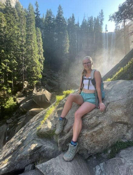 Myself sitting on a rock in Yosemite National Park with a waterfall behind me.