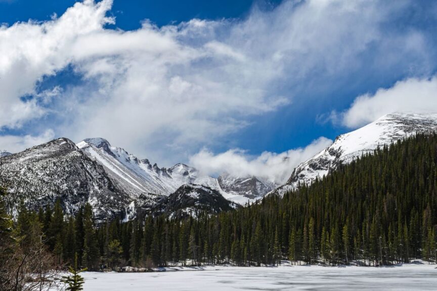 Snow capped peaks towering above a frozen lake on a sunny day at Rocky Mountain National Park.